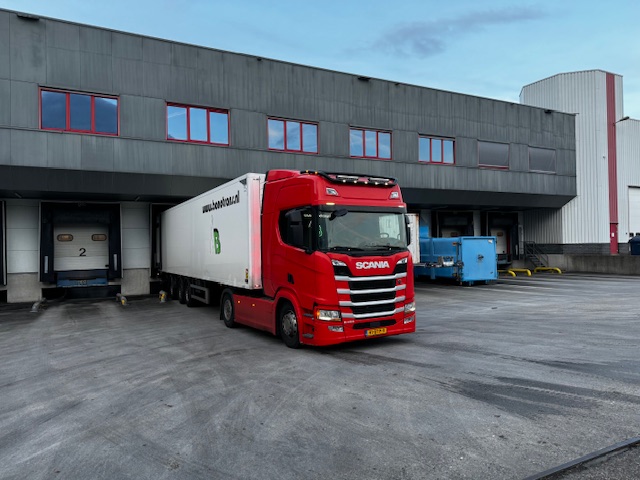 Rode Scania met Bonotrans-oplegger bij een distributiecentrum